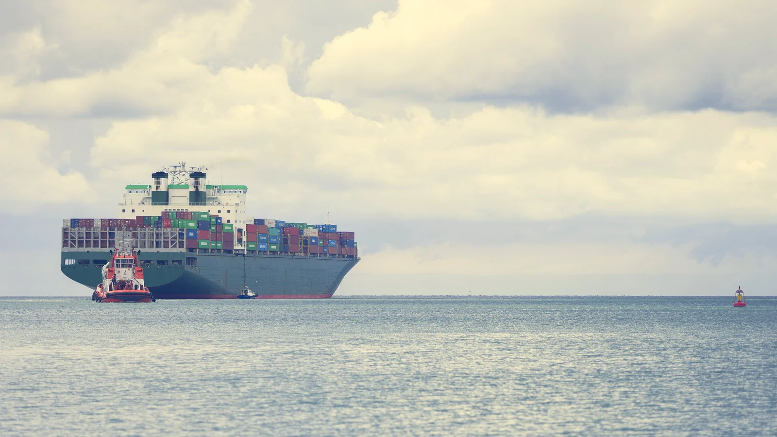 Loaded container ship with a tug approaching port across calm open water