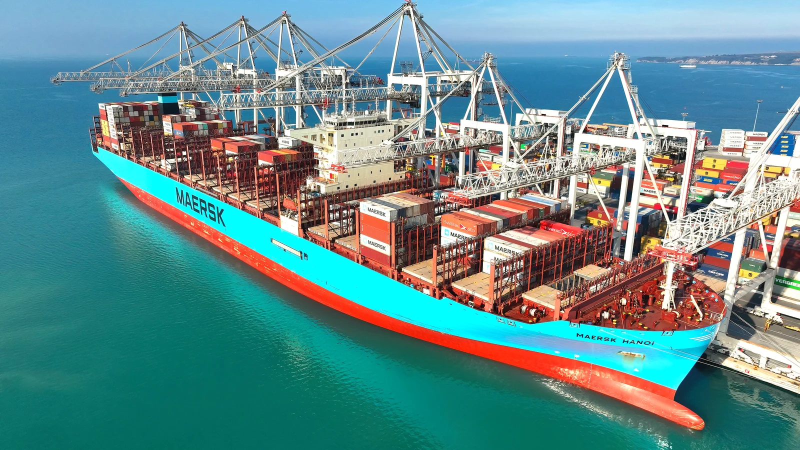 Light-blue Maersk container ship moored at a terminal under gantry cranes, turquoise water