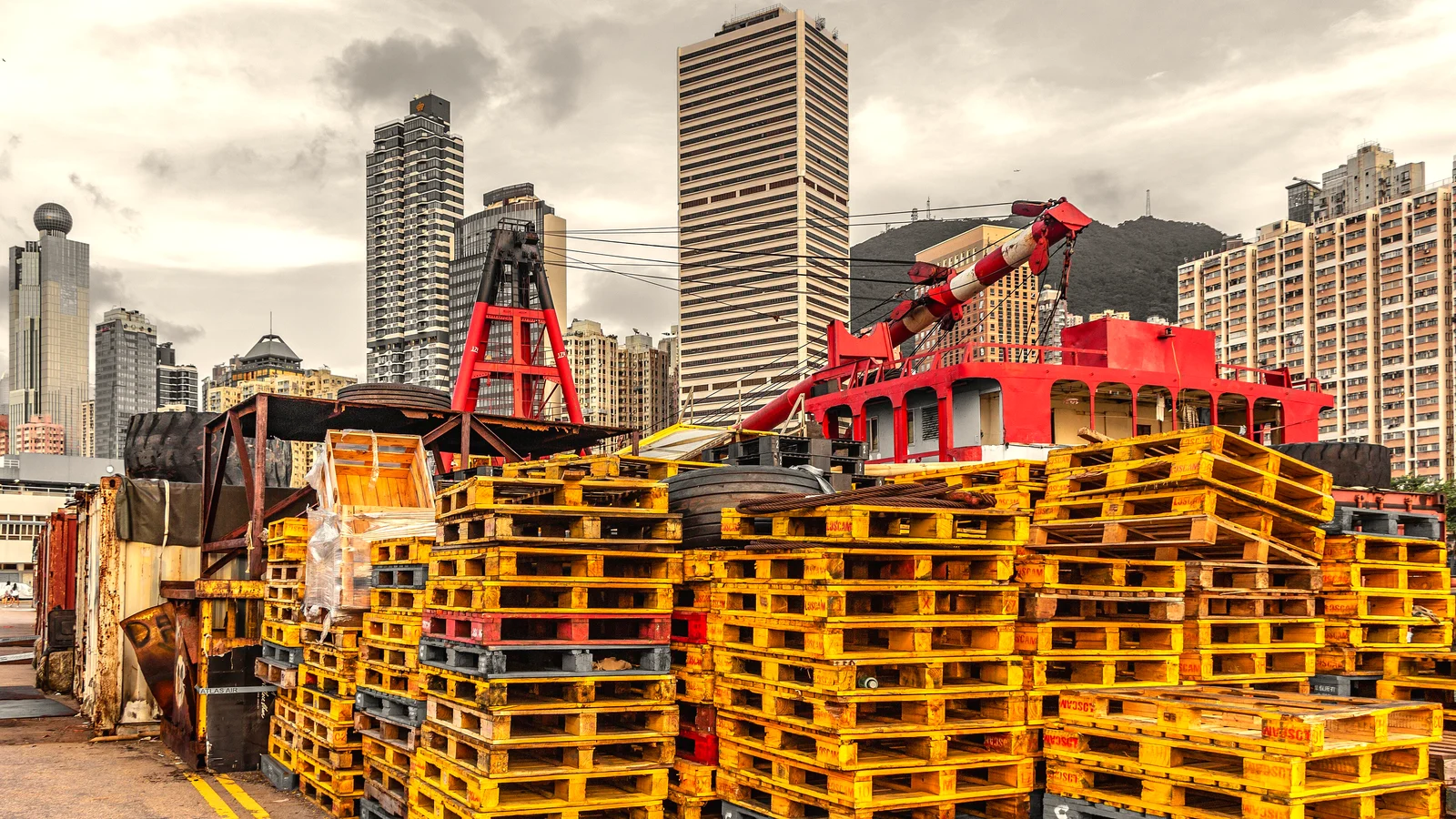 Stacks of yellow wooden pallets at a harbour cargo area with city towers behind
