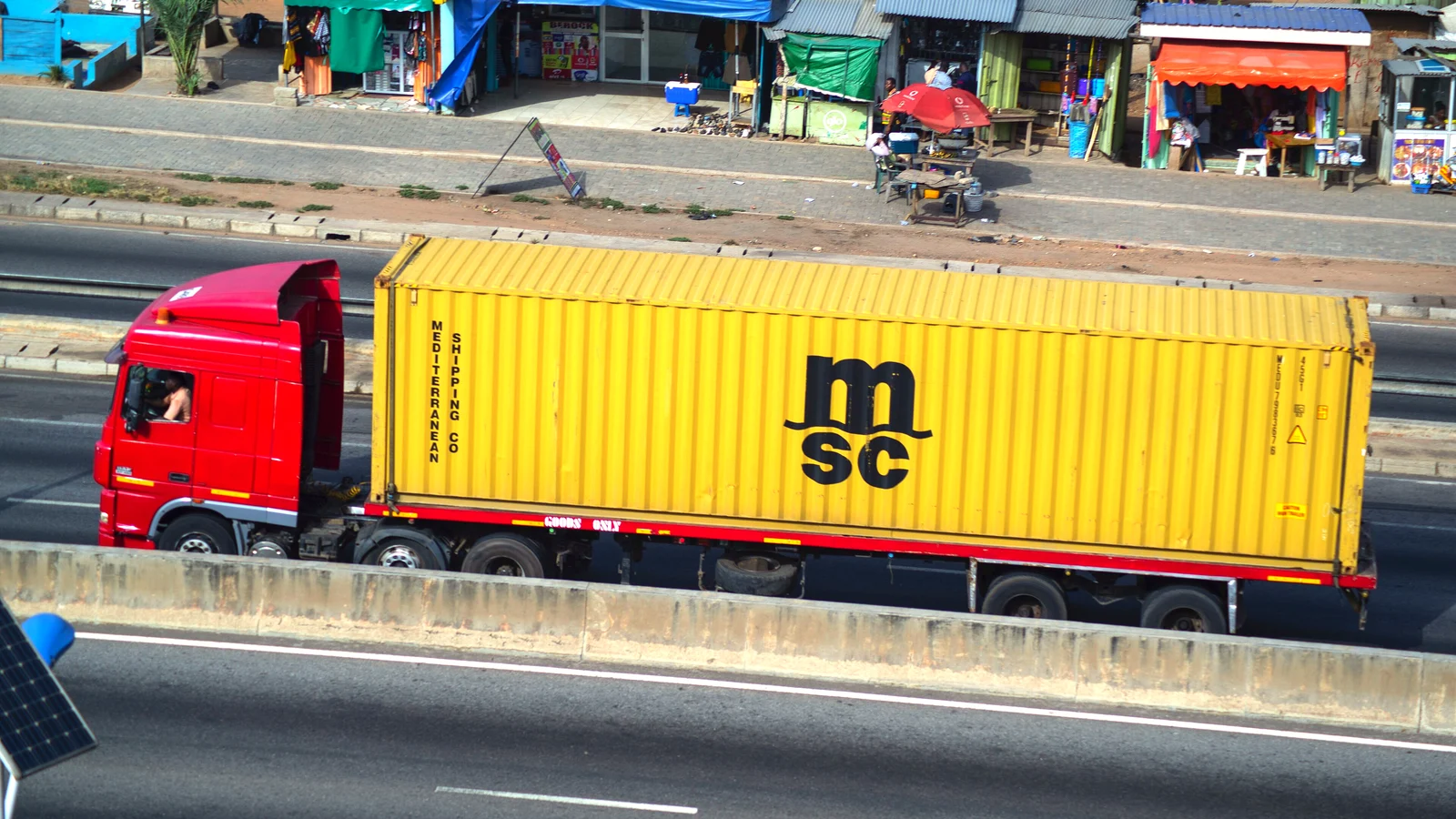 Red truck hauling a yellow 40ft MSC container along a highway in daylight