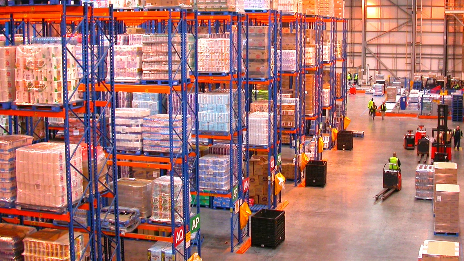 Distribution centre aisles with pallet racks of stocked goods and forklifts at work