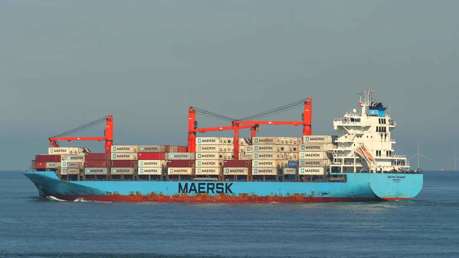 Blue Maersk container ship with red cranes sailing at sea, fully in frame